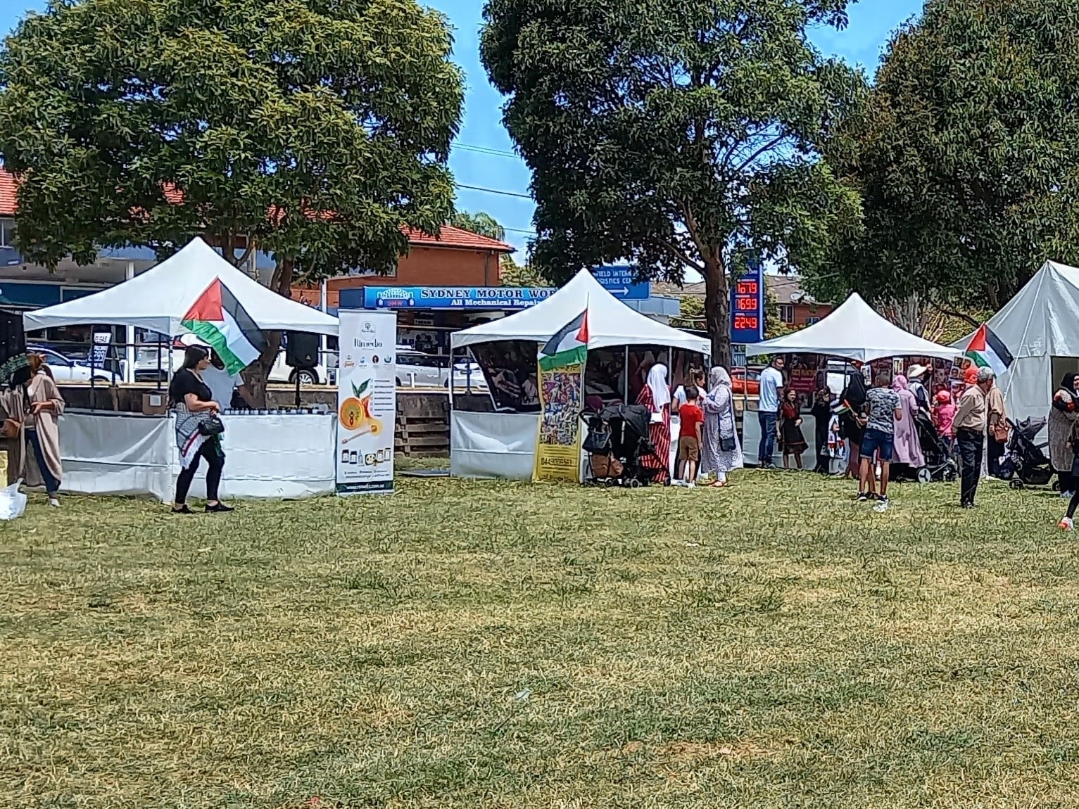 Families walking between the white stall tents on the grass, with Palestinian flags flying